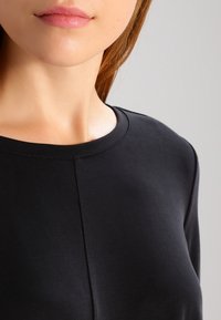 Svart topp med rund halsringning i ett mjukt tyg. Har en diskret sömdetalj fram, med åtsittande långa ärmar.