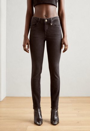 Sort slim-fit jeans med guldknap og lynlås, båret med sorte ankelstøvler og cropped sort top, vist fra talje til fødder.