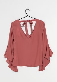 Blouse rosée avec un décolleté en V profond et une fermeture à nouer dans le dos. Comprend des manches longues évasées et une texture de tissu lisse et légère.