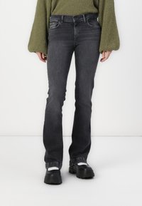 Jean flared en denim gris avec cinq poches, passants de ceinture et légère décoloration. Associé à des chaussures à plateforme noires et un pull en tricot vert.