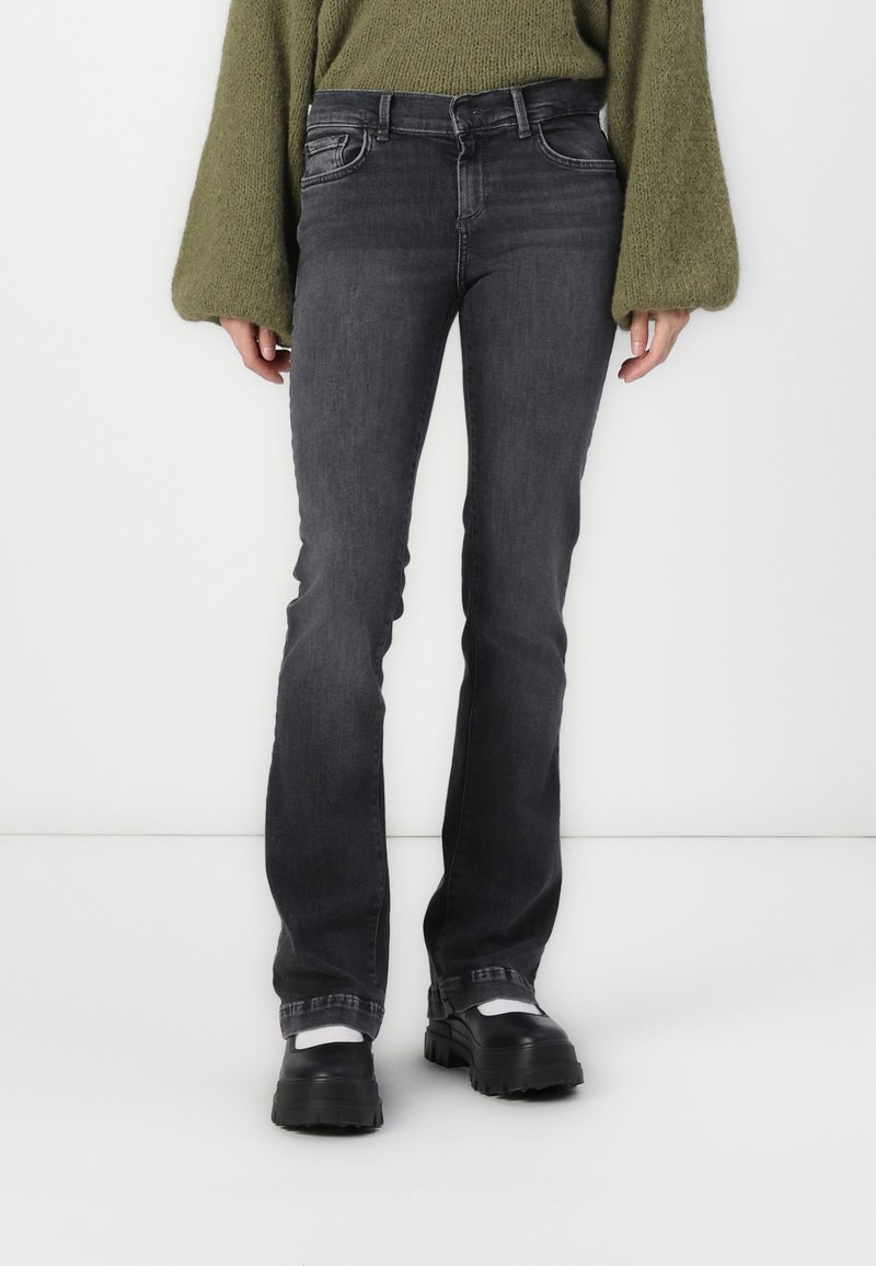 Jean flared en denim gris avec cinq poches, passants de ceinture et légère décoloration. Associé à des chaussures à plateforme noires et un pull en tricot vert.