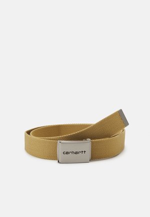 Tan geweven stoffen riem opgerold met een matte zilveren metalen gesp gegraveerd met het Carhartt-logo.