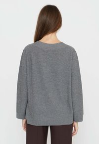 Maglione grigio di lana con vestibilità ampia, scollo rotondo e spalle scese; presenta una texture minimale ed è abbinato a pantaloni marroni.