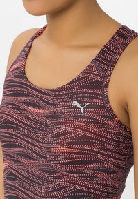 Puma urheilusukkapaita tummalla taustalla, jossa on vaaleanpunaisia pistekuvioita. Tyylikäs, istuva muotoilu leveillä olkaimilla ja logo edessä.