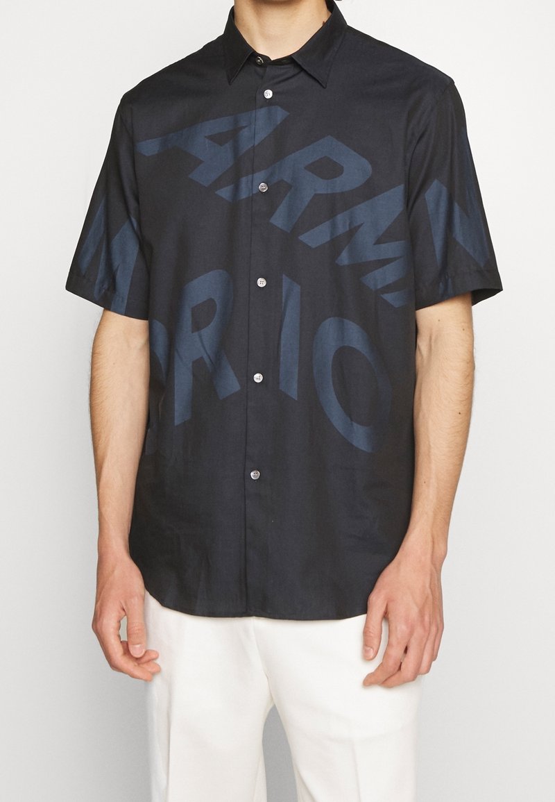 Kratké rukávy košile z tmavě námořnického materiálu, která představuje velký tónový grafický design s textem. Zapínání na knoflíky a detail límce. Texturovaná tkanina.