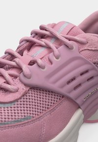 Κοντινό πλάνο ροζ αθλητικού αθλητικού παπουτσιού με ύφασμα από δίχτυ, επενδεδυμένο γιακά, χονδρά κορδόνια και χυτό πλαστικό στήριγμα πάνω από το μέσο του ποδιού με τη σήμανση "Jordan".