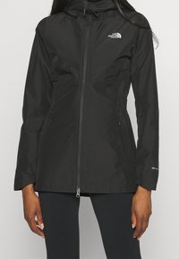 Chaqueta impermeable negra con capucha, cierre de cremallera, cintura elastizada y bolsillos laterales. Presenta el logo "The North Face" en el pecho.