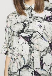 Skjorta med knappar som har en vit bas med ett svart och färgglatt abstrakt stenmönster. Korta ärmar, lätt tyg och en klassisk krage.