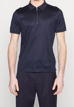 Polo bleu marine avec un col zippé, des manches courtes et une texture lisse. Il présente un col classique et une étiquette de marque discrète à l'ourlet.