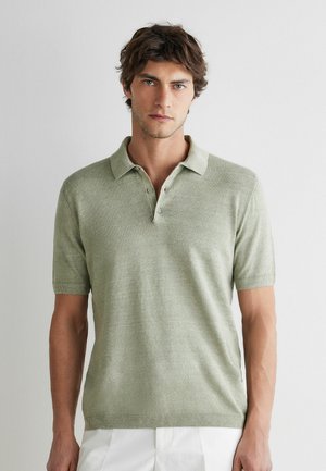 Ung mand med kort brunt hår iført en lysegrøn kortærmet poloshirt og hvide bukser mod en ensfarvet hvid baggrund.