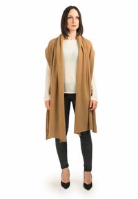 Brun, uldlignende omslag med en blød tekstur, ligger over en lys sweater og sorte jeans. Passer til spidse sorte hæle, hvilket forbedrer outfitets silhuet.