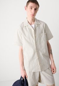 Short-sleeve collared shirt and shorts set in cream with thin blue stripes. Features a left chest pocket and smooth fabric texture.