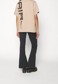 Beige bomulls t-shirt med ett stort mörkbrunt "AIR" tryck på ryggen, kombinerad med svarta utsvängda byxor och kraftiga svarta stövlar.