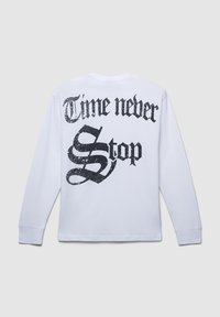 Biała koszulka z długim rękawem z dużym czarnym tekstem na plecach: "Czas nigdy się nie zatrzymuje", z teksturowanym wzorem graficznym.