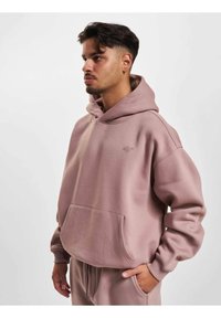Lyserød bomulds hoodie med en frontlomme og snøre i hætten. Har et diskret logo på brystet og ribbede manchetter. Blød tekstur.