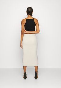 Svart ärmlös topp som är kombinerad med en ribbad ljusgrå kjol i knälängd; modellen bär svarta högklackade skor; slät textur, figurnära design.