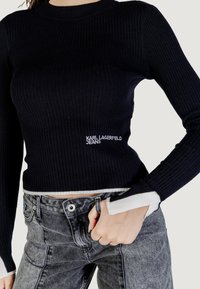 Pull en tricot noir ajusté à côtes avec des accents blancs aux manches et un logo brodé "KARL LAGERFELD JEANS" à la taille.