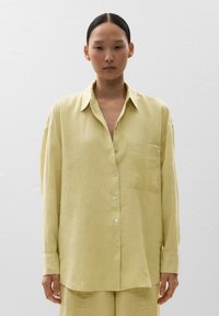 Camicia lunga a maniche giallo chiaro in lino. Presenta una chiusura con bottoni sul davanti, una tasca sul petto e una vestibilità rilassata. Tessuto morbido e leggero.