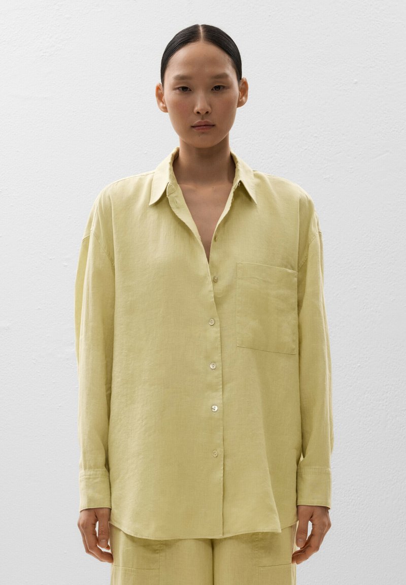 Camicia lunga a maniche giallo chiaro in lino. Presenta una chiusura con bottoni sul davanti, una tasca sul petto e una vestibilità rilassata. Tessuto morbido e leggero.