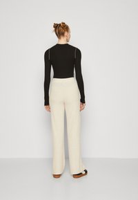 Top nero a maniche lunghe con cuciture chiare, abbinato a pantaloni larghi color crema in un tessuto testurizzato, completato da calzature scure.
