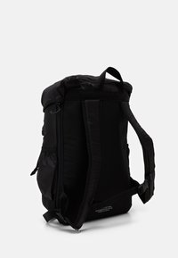 Černý batoh s polstrovaným zádovým panelem a popruhy, vybavený horním poutkem, bočními kapsami a zipovým uzavřením, vyrobený z odolné tkaniny.