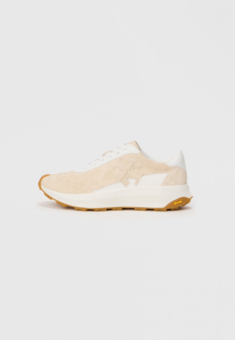 Beige semsket sneakers med hvite detaljer, rund tå, snøring, og teksturert gummisåle med Vibram-merke.