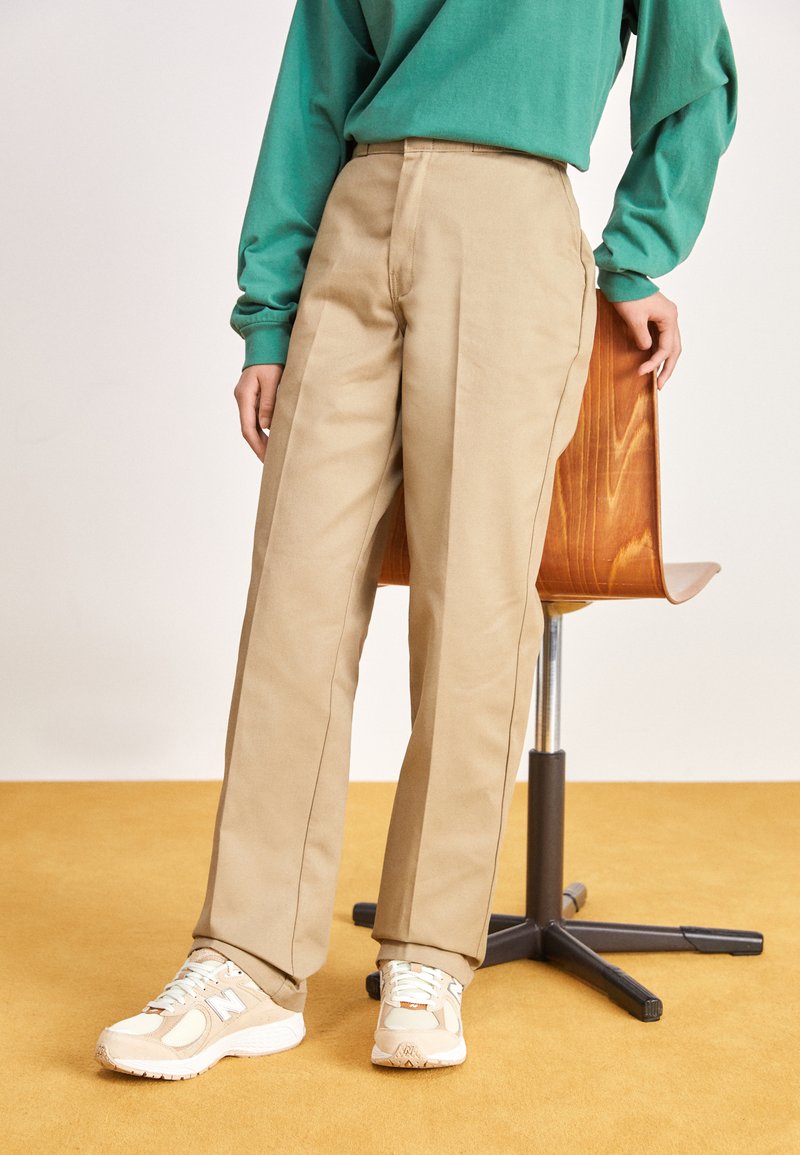 Pantaloni beige con un design a gamba dritta, caratterizzati da una texture liscia e dettagli nella cucitura laterale, abbinati a sneakers di colore chiaro.
