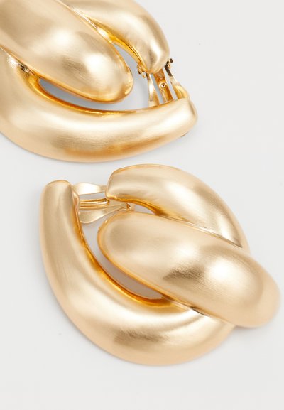 Gouden metalen oorbellen met een glad, gedraaid ontwerp en een gepolijste afwerking, voorzien van een veilige sluiting. Geweven accenten zijn zichtbaar.