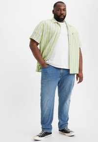 Camisa de manga corta a rayas de varios colores en verde claro, amarillo y azul, combinada con jeans de mezclilla azul y zapatillas negras.