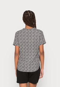 Short-sleeve shirt in black and white floral print, made of lightweight fabric. Features a rounded hem and relaxed fit. Paired with black shorts.
