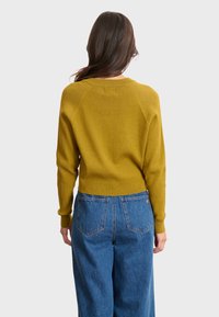 Senapsgul stickad tröja med ribbad textur, åtsittande ärmslut och rundad nederkant, tillsammans med högmidjade blå denimjeans.