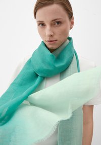 Écharpe turquoise et vert clair en tissu léger, présentant une texture douce et des bords effilochés, enroulée autour du cou du modèle.