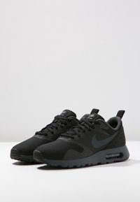 Ett par svarta Nike Air Max-sneakers med textilstruktur, snörningsdesign och synlig luftdämpning på vit yta.