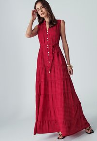 Červené maxi šaty s vrstveným dizajnom, s gombíkovou prednou časťou, golierovým výstrihom a opaskom v páse. Vyrobené z textúrovanej látky.