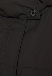 Czarna pikowana kurtka o gładkiej fakturze tkaniny, z dużym kołnierzem i zapięciem na guziki z czterema dziurkami.