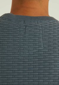 Knitted sweater in dark blue with a textured checkered pattern. Features a ribbed collar and a small loop detail at the back.