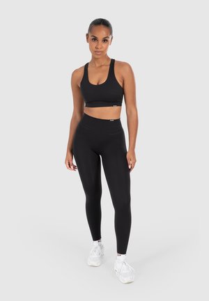 Schwarzer Sport-BH und Leggings aus dehnbarem Material. Der BH hat breite Träger und die Leggings verfügen über einen hohen Bund.