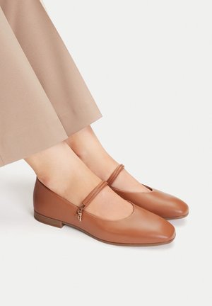 Brązowe baleriny ze skóry z zaokrąglonym noskiem i niskim obcasem, ozdobione dekoracyjnym paskiem i małym zawieszonym dodatkiem z boku.
