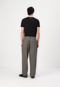 Zwarte t-shirt en lichtgrijze wijde broek. De t-shirt heeft een ronde hals, de broek heeft twee achterzakken en een gladde textuur.