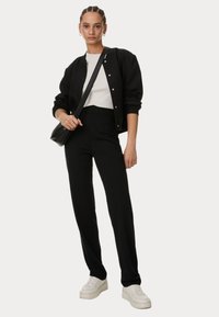 Černá bomber bunda se stříbrnými patentkami, bílý přiléhavý top, černé kalhoty s vysokým pasem a bílé tenisky. Jednoduchý design, minimalistický styl.