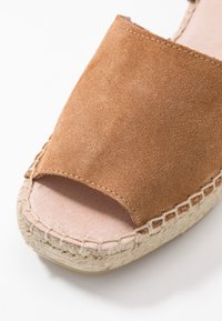 Hnědé semišové espadrilky s otevřenou špičkou a juteovou podrážkou, s růžovým vnitřním podšíváním; obsahují prošívané akcenty kolem základny.