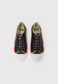 Čierne a červené nízke tenisky s bielymi gumovými špičkami, vybavené šnúrkami, zosilneným šitím a textúrovaným vrchným materiálom z látky. Logo viditeľné vo vnútri.