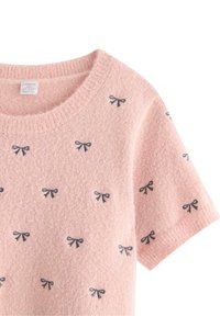 Lyserød strikket sweater med korte ærmer og en rund halsudskæring, der er prydet med små sorte sløjfemønstre overalt.
