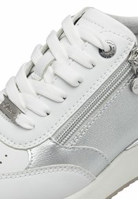 Fehér sneaker sima bőr felső résszel, ezüst fémes részletekkel, szövettextúrával, fehér cipőfűzőkkel és dekoratív cipzár részlettel az oldalon.