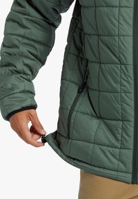 Padded green jacket with a quilted pattern, zipper pockets, and an adjustable hem. The sleeve features a black cuff accent.