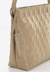 Borsa a mano in pelle beige con un design testurizzato caratterizzato da motivi triangolari in rilievo. La ferramenta dorata valorizza l'etichetta del brand. Tracolla regolabile.