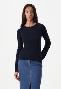Pull en maille côtelée bleu marine à manches longues avec un col rond, design ajusté et texture lisse, associé à une jupe en denim avec fente avant.