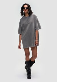 Przesadnie duża szara sukienka T-shirt o miękkiej fakturze i krótkich rękawach, zestawiona z czarnymi kozakami do kolan i prostokątnymi czarnymi okularami przeciwsłonecznymi.