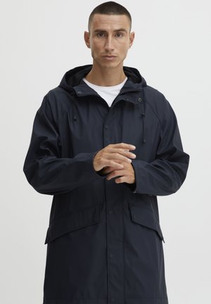 Navy waterproof jacket with hood, front snap buttons, and two side pockets. Smooth texture, relaxed fit, and adjustable drawstrings on hood.