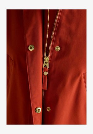 Red jacket featuring a gold zipper and snap buttons, made of smooth fabric with a slightly textured finish. Close-up view highlighting details.